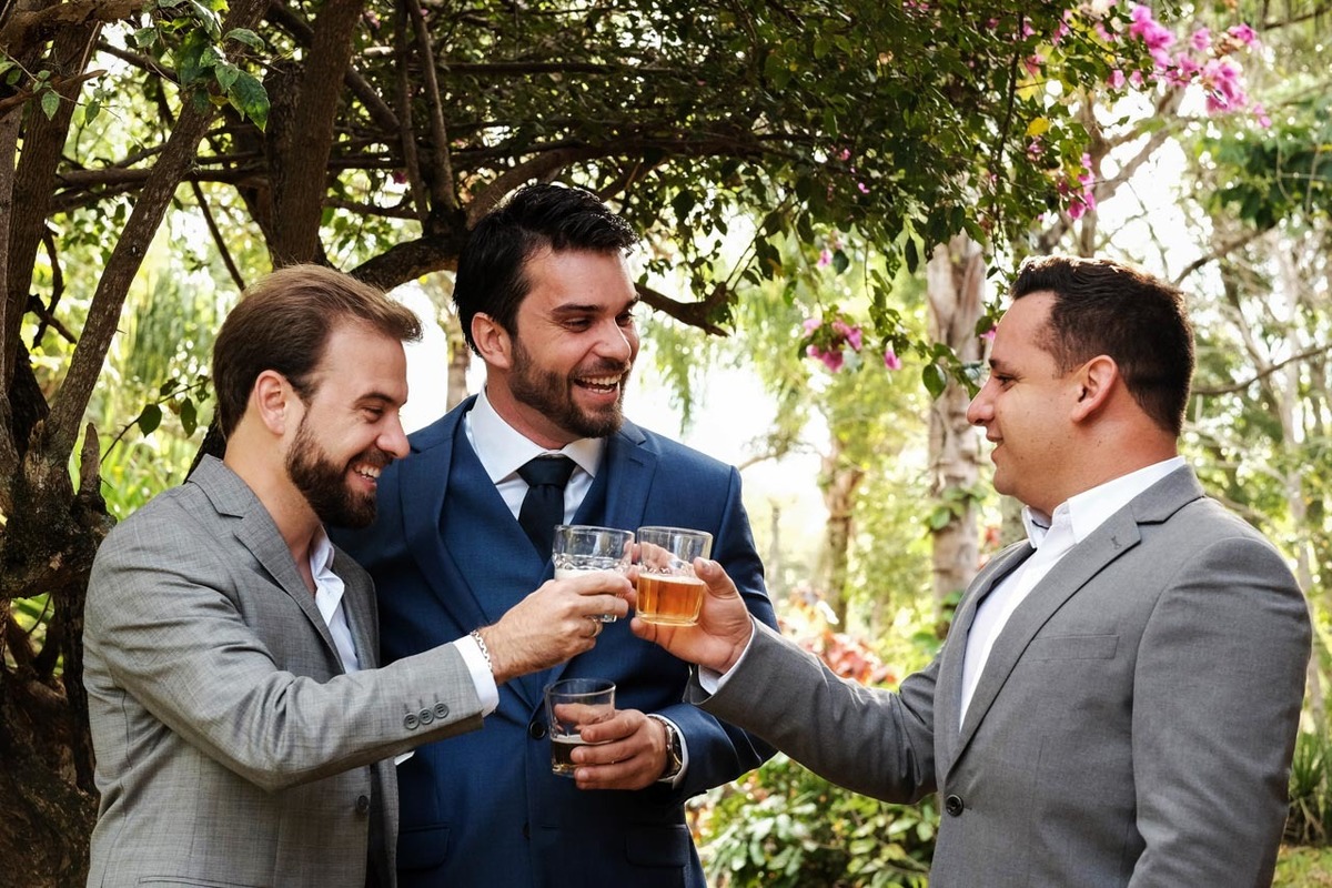noivo brinca muito feliz com padrinhos tomando uma cerveja sorrindo em meio a natureza em casamento lindo no pôr do sol no hotel fazenda sete lagos em Guaratinguetá fotos erasmo ballot
