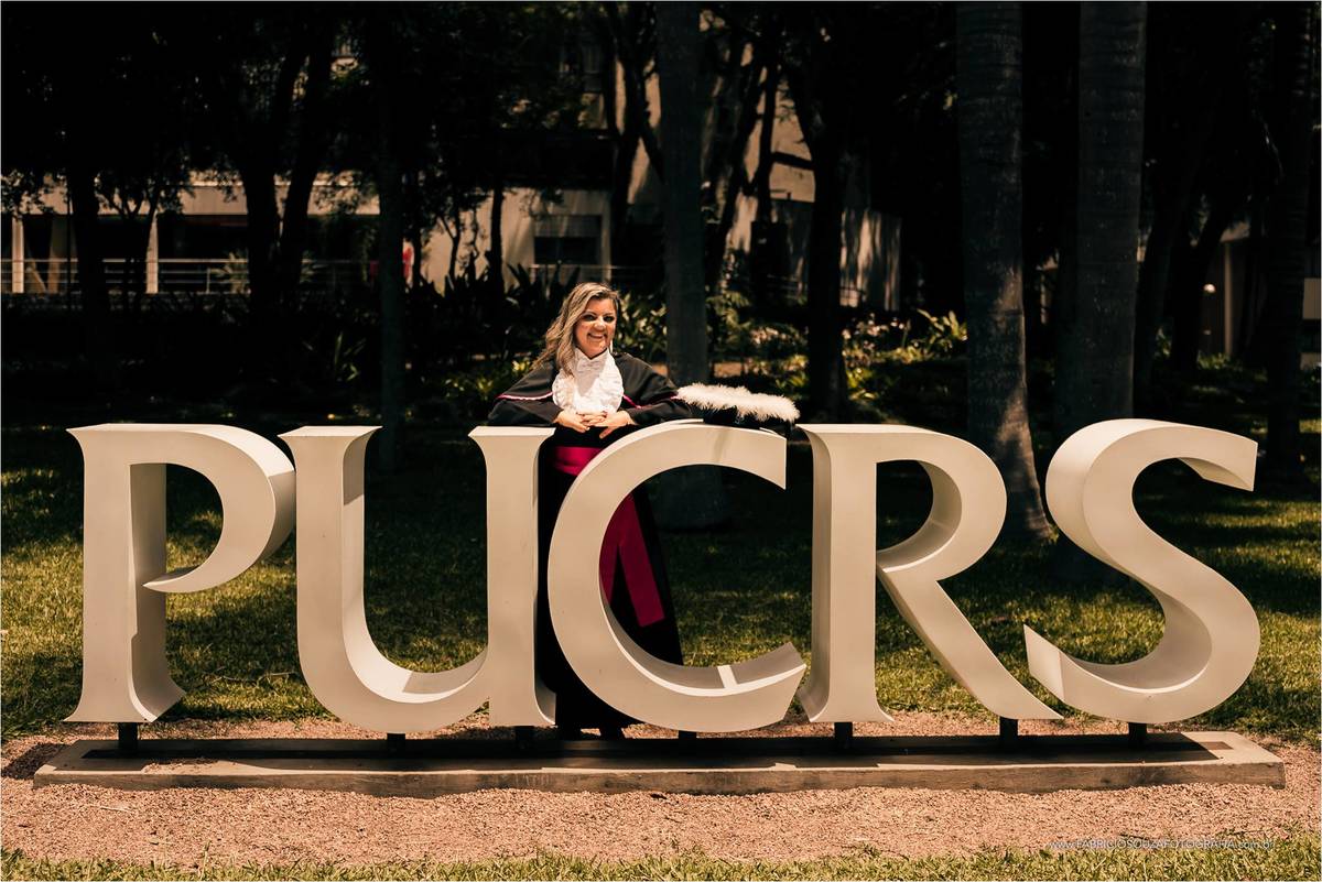 Rosangela posando para foto em frente ao letreiro da PUCRS no pátio do campus