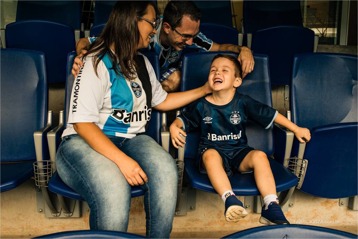 familia feliz nas cadeiras da arena do gremio, todos fardados com o uniforme do imortal tricolor