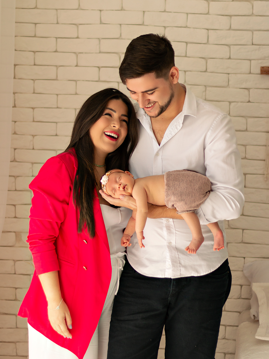 Foto de bebê recém-nascida coberta com tecido sendo segurada pelos pais. Ensaio Newborn em Estúdio Natal/RN.