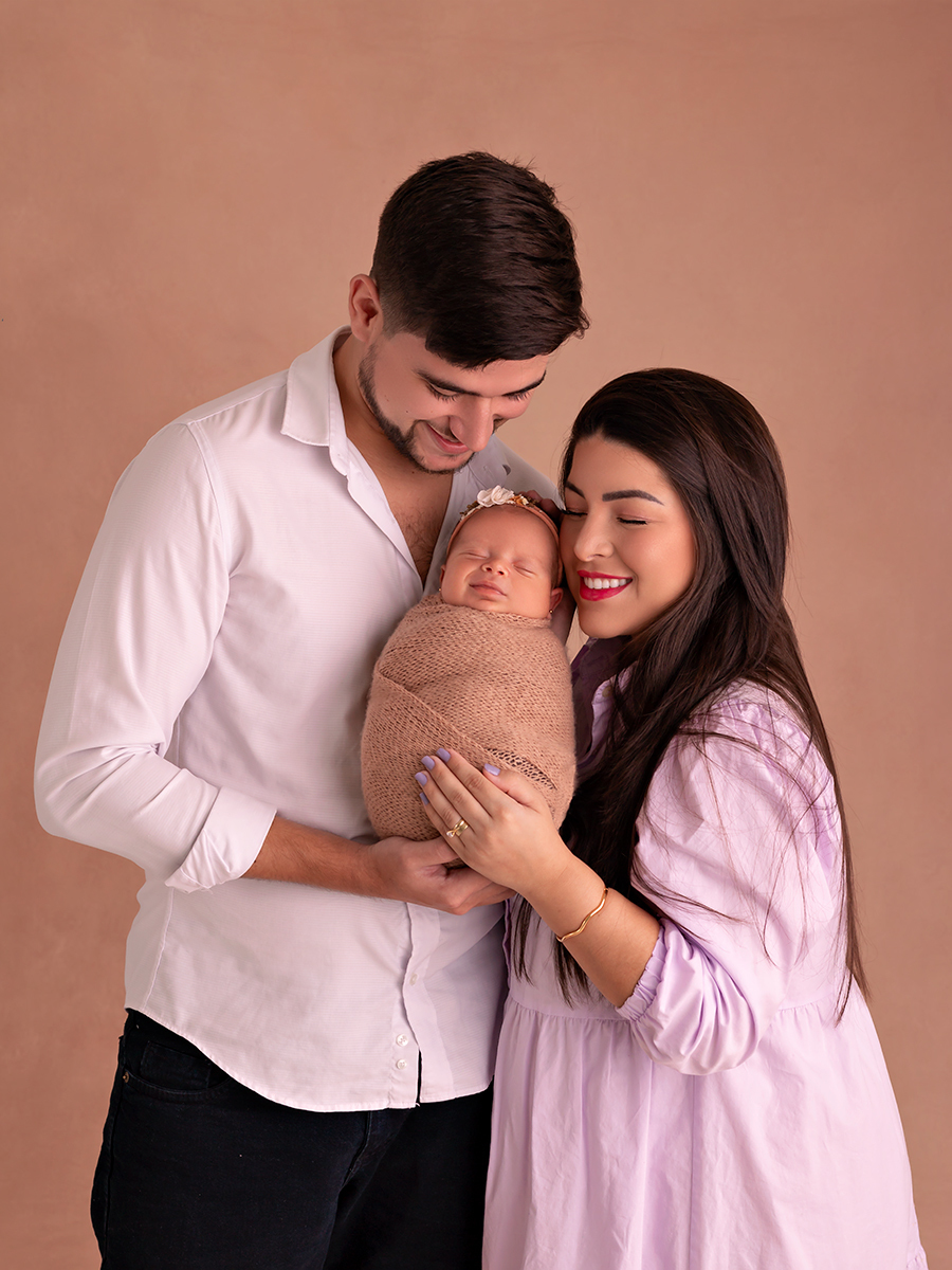Foto de bebê recém-nascida enrolada em wrap sendo segurada pelos pais. Ensaio Newborn em Estúdio Natal/RN.