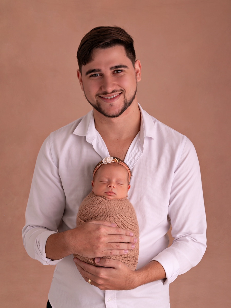 Foto de bebê recém-nascida enrolada em wrap sendo segurada pelo pai. Ensaio Newborn em Estúdio Natal/RN.