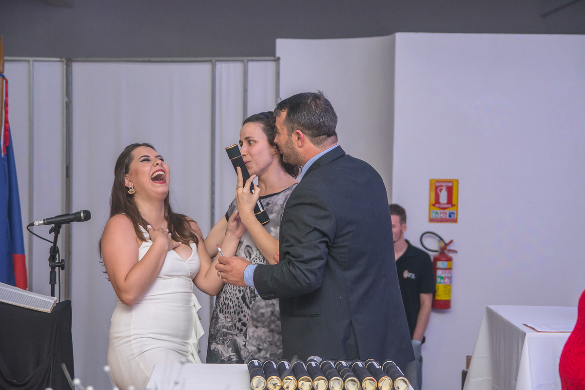 Formanda rindo com professores enquanto recebe o diploma