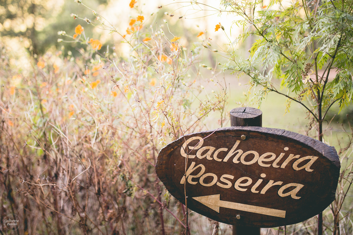 Ensaio pré casamento de Guilherme Santos Fotografia que rolou no recanto das cachoeiras em Brotas-SP, sessão fotográfica no final de tarde, placa indicando o local da cachoeira no meio da natureza.