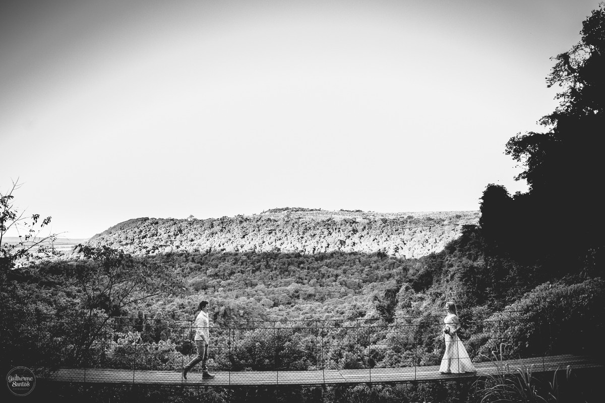 Fotografia de pré casamento feita no final de tarde pelo fotógrafo Guilherme Santos, casal de noivos caminhando em uma ponte suspensa em Brotas, sessão de fotos pré casamento na natureza.