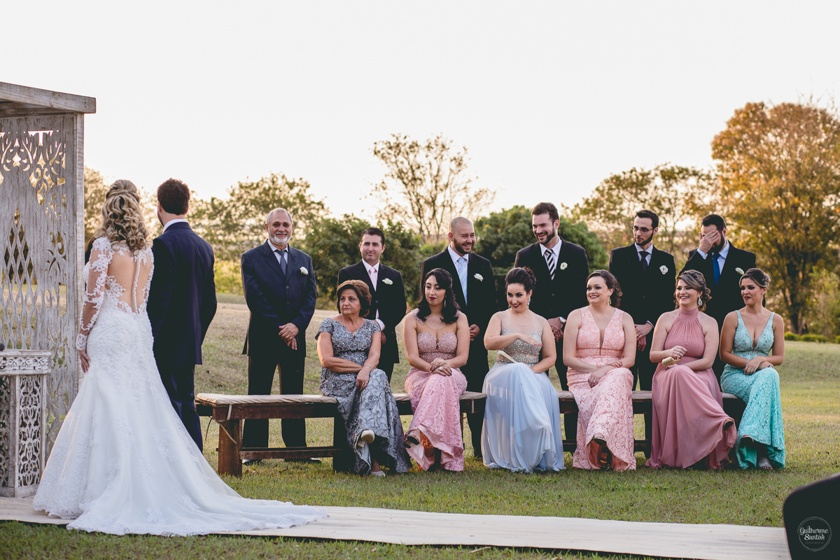 Fotografia de casamento pelo fotógrafo Guilherme Santos, madrinhas e padrinhos olhando os noivos durante a cerimônia de casamento com pôr do sol em Pederneiras.