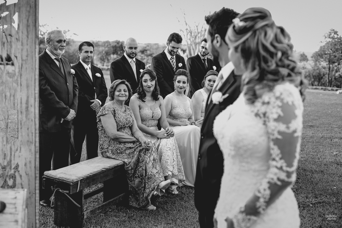 Fotografia de casamento pelo fotógrafo Guilherme Santos, madrinhas e padrinhos sorrindo e olhando os noivos durante a cerimônia de casamento ao ar livre em Pederneiras.