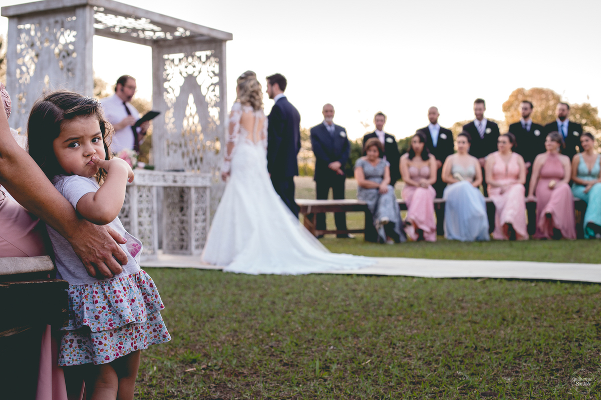 Fotografia de casamento pelo fotógrafo Guilherme Santos, criança durante a cerimônia de casamento ao ar livre em Pederneiras. Casamento com pôr do sol.