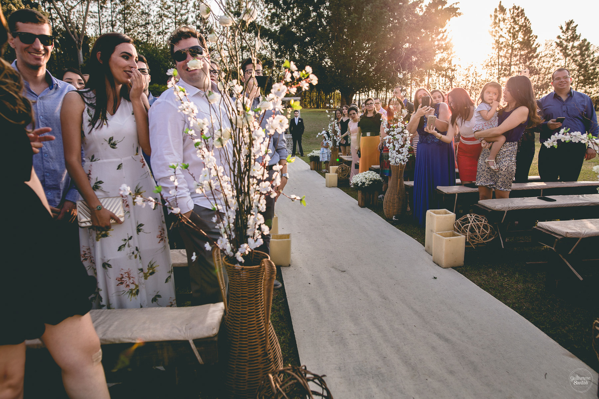Fotografia de casamento pelo fotógrafo Guilherme Santos, convidados olhando a noiva entrar na cerimônia de casamento no fim de tarde em Pederneiras.