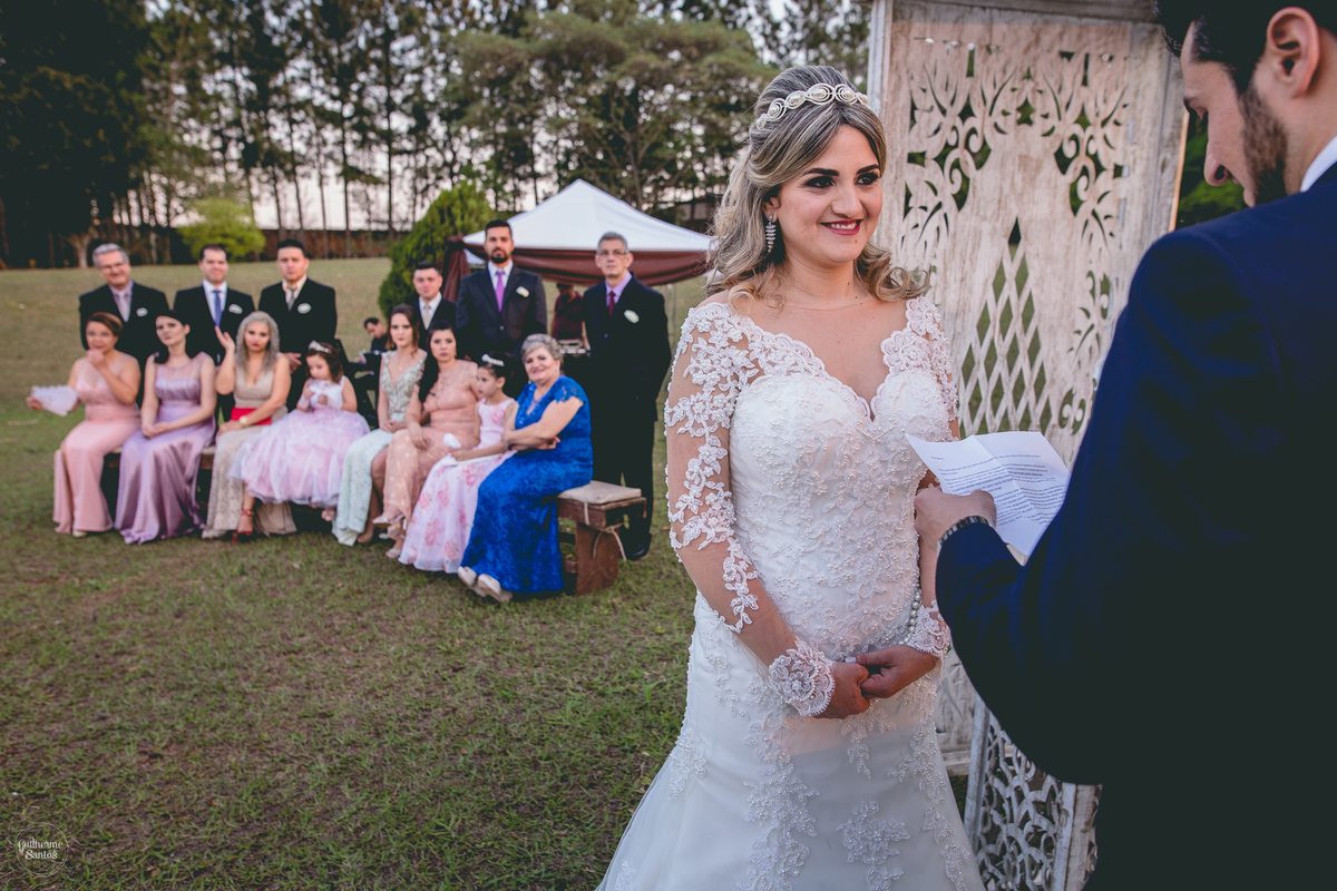 Fotografia de casamento pelo fotógrafo Guilherme Santos, noiva sorrindo para o noivo durante os votos na cerimônia de casamento ao ar livre.