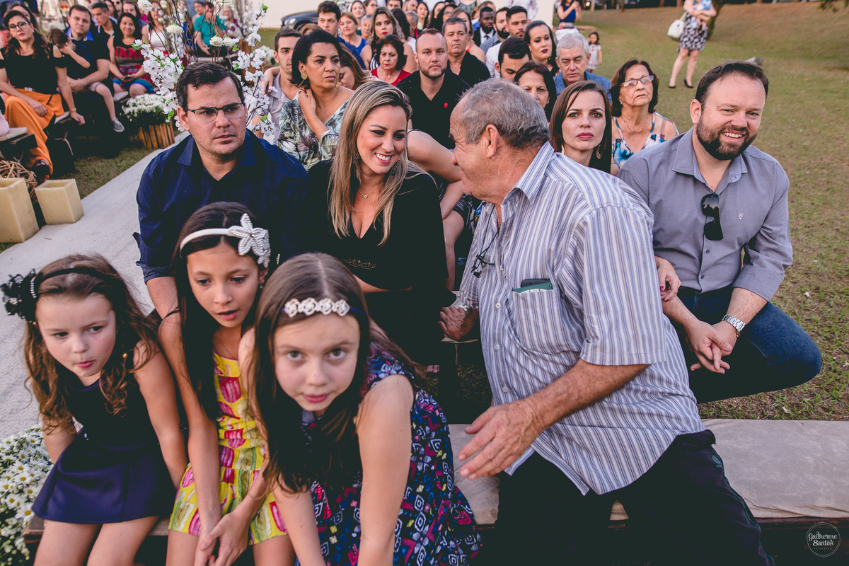 Fotografia de casamento pelo fotógrafo Guilherme Santos, convidados do casamento olhando durante o casamento ao ar livre. Crianças na cerimônia de casamento em Pederneiras.