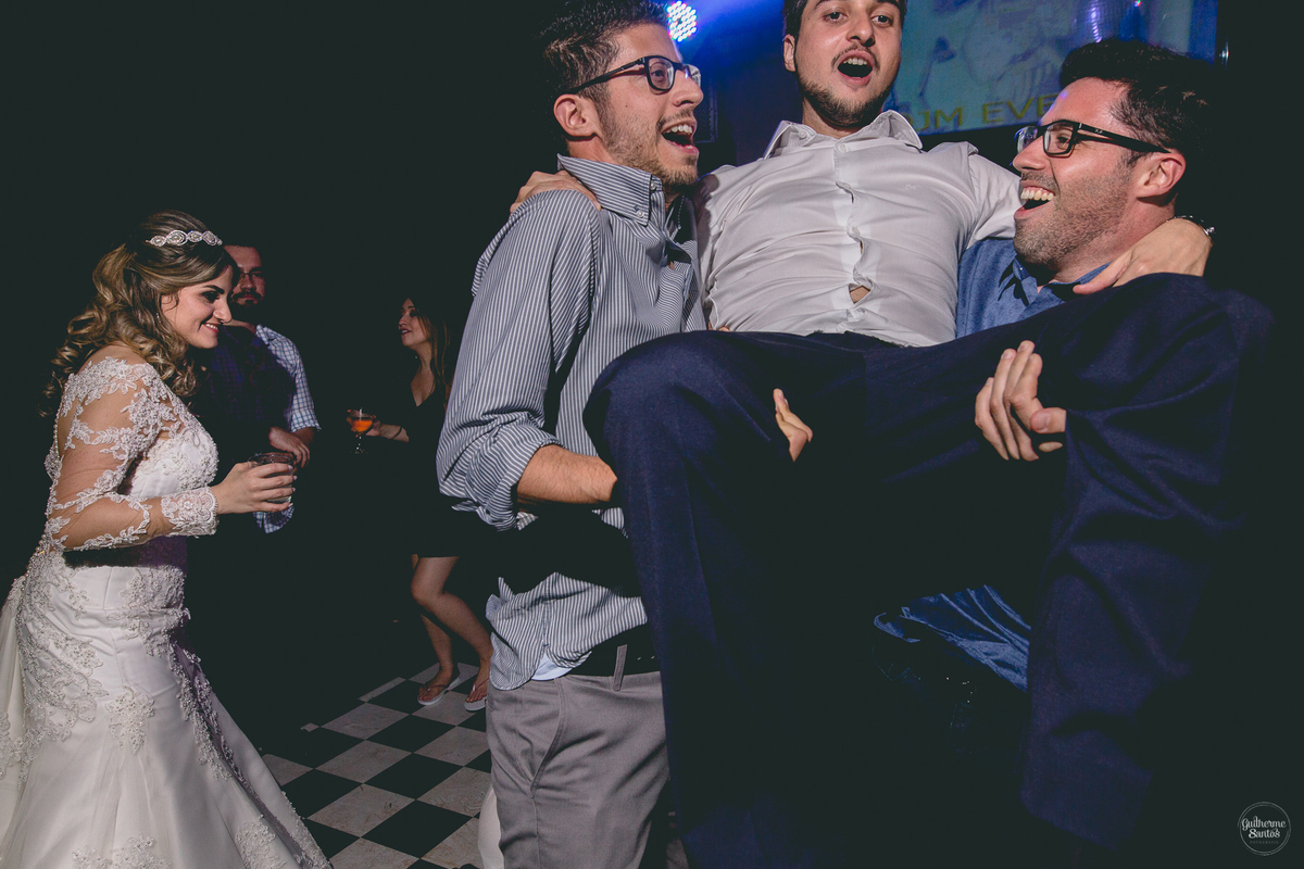 Fotografia de casamento pelo fotógrafo Guilherme Santos, noivo levantado no alto pelos padrinhos durante a festa de casamento ao ar livre.