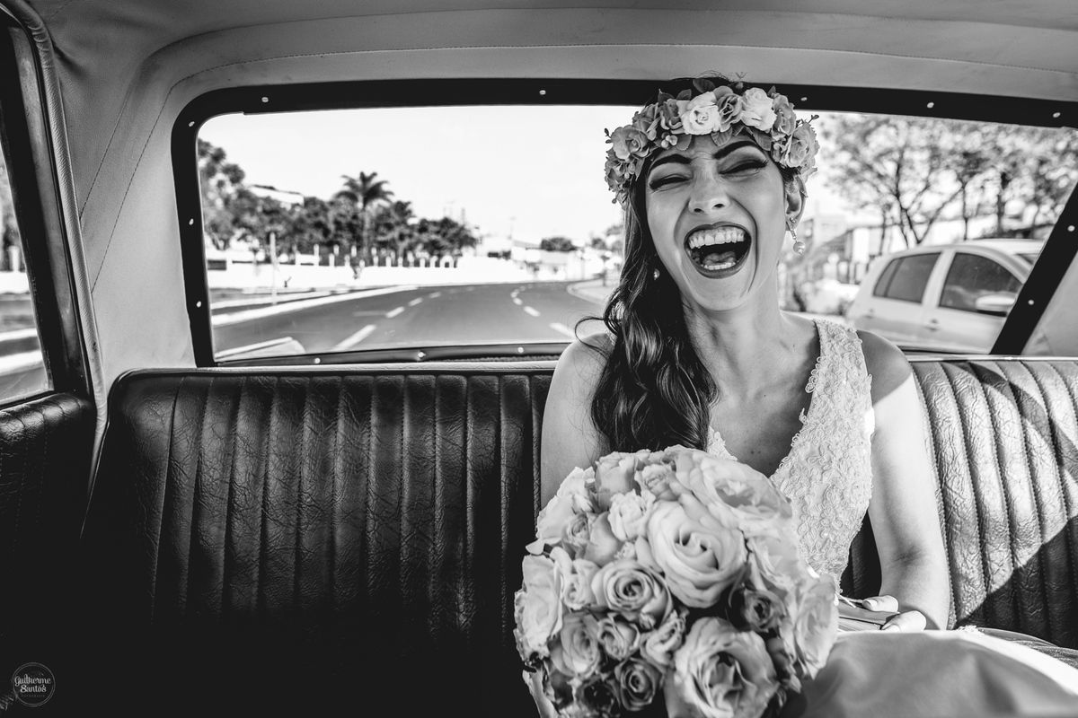 Fotografia de casamento feita pelo fotógrafo Guilherme Santos, noiva sorrindo feliz com seu buquê de flores, noiva está em um carro antigo se dirigindo ao casamento durante o dia em Bauru.