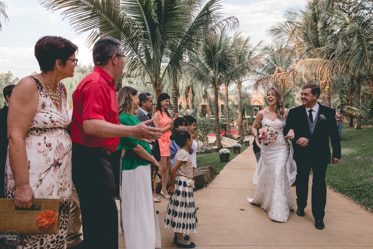 Fotografia de casamento feita no final de tarde pelo fotógrafo Guilherme Santos, noiva entrando na capela com seu pai. Noiva sorrindo para os convidados no casamento ao ar livre em Botucatu.