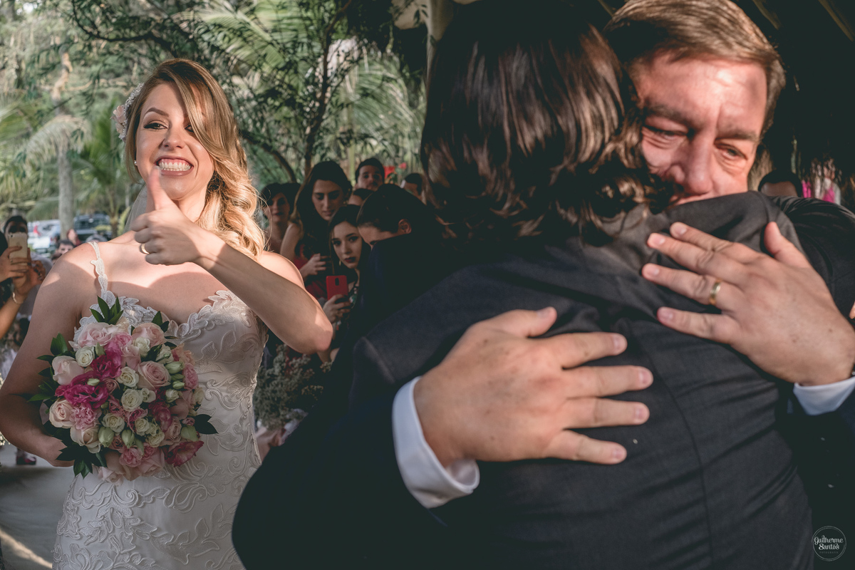 Fotografia de casamento feita no final de tarde pelo fotógrafo Guilherme Santos, pai da noiva cumprimentando o noivo. Noiva está segurando o buquê de flores.