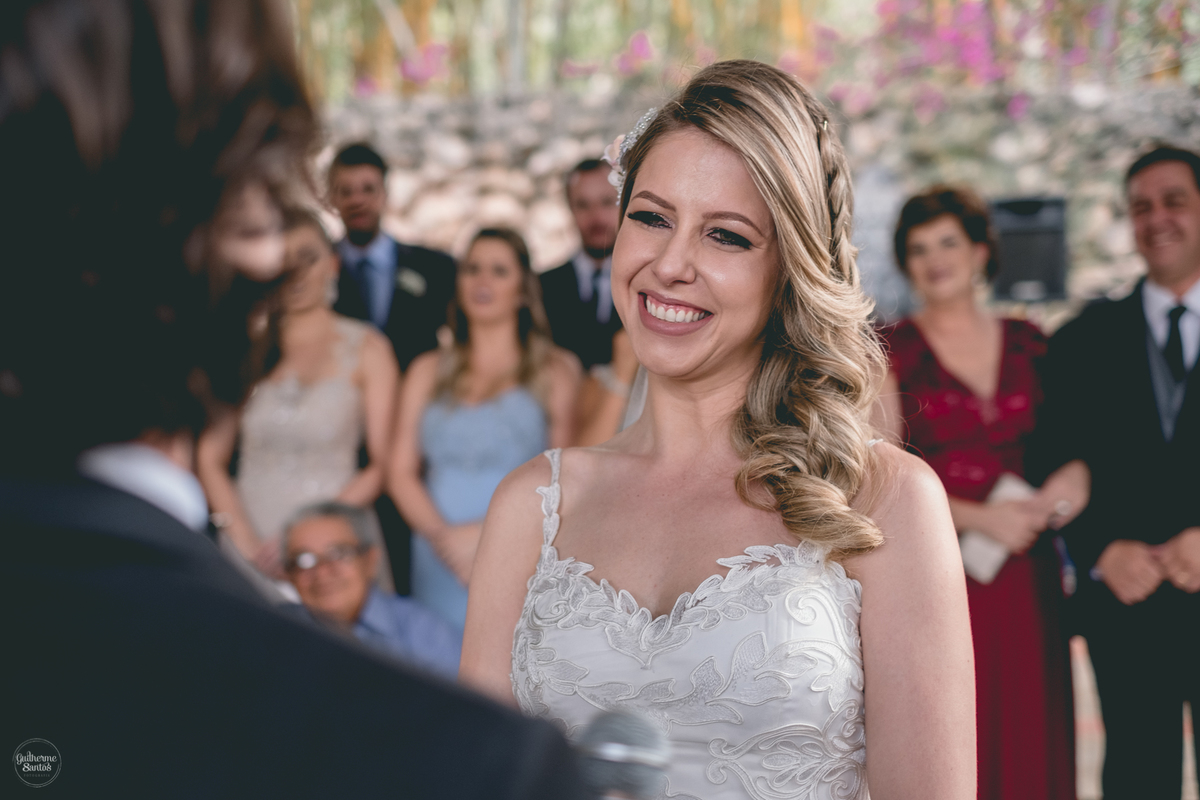 Fotografia de casamento feita no final de tarde pelo fotógrafo Guilherme Santos, noiva sorrindo para o noivo na hora dos votos no casamento ao ar livre em Botucatu.