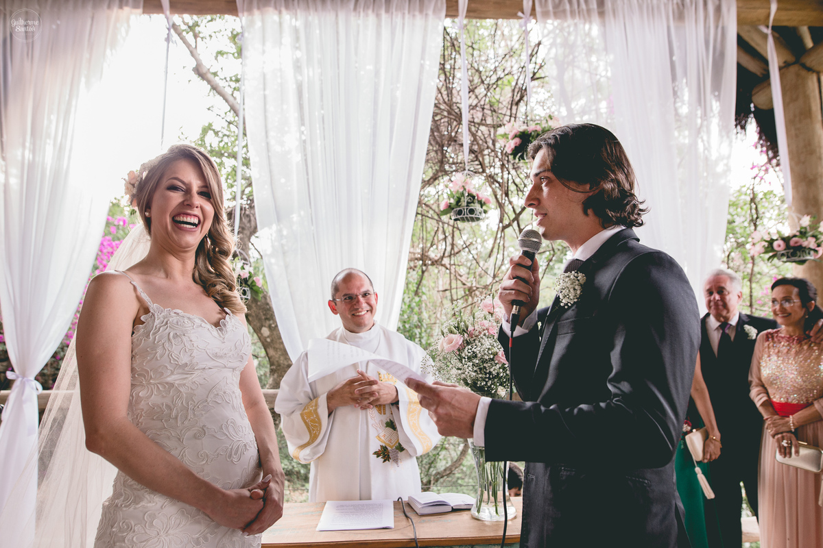 Fotografia de casamento feita no final de tarde pelo fotógrafo Guilherme Santos, noivo falando os votos para a noiva no casamento ao ar livre em Brotas. Convidados felizes.