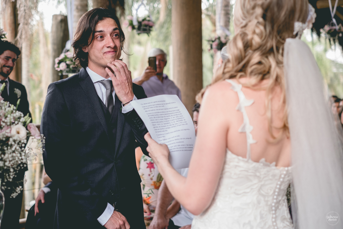 Fotografia de casamento feita no final de tarde pelo fotógrafo Guilherme Santos, noiva lendo os votos para o noivo no casamento ao ar livre em Botucatu. Noiva com véu e grinalda.