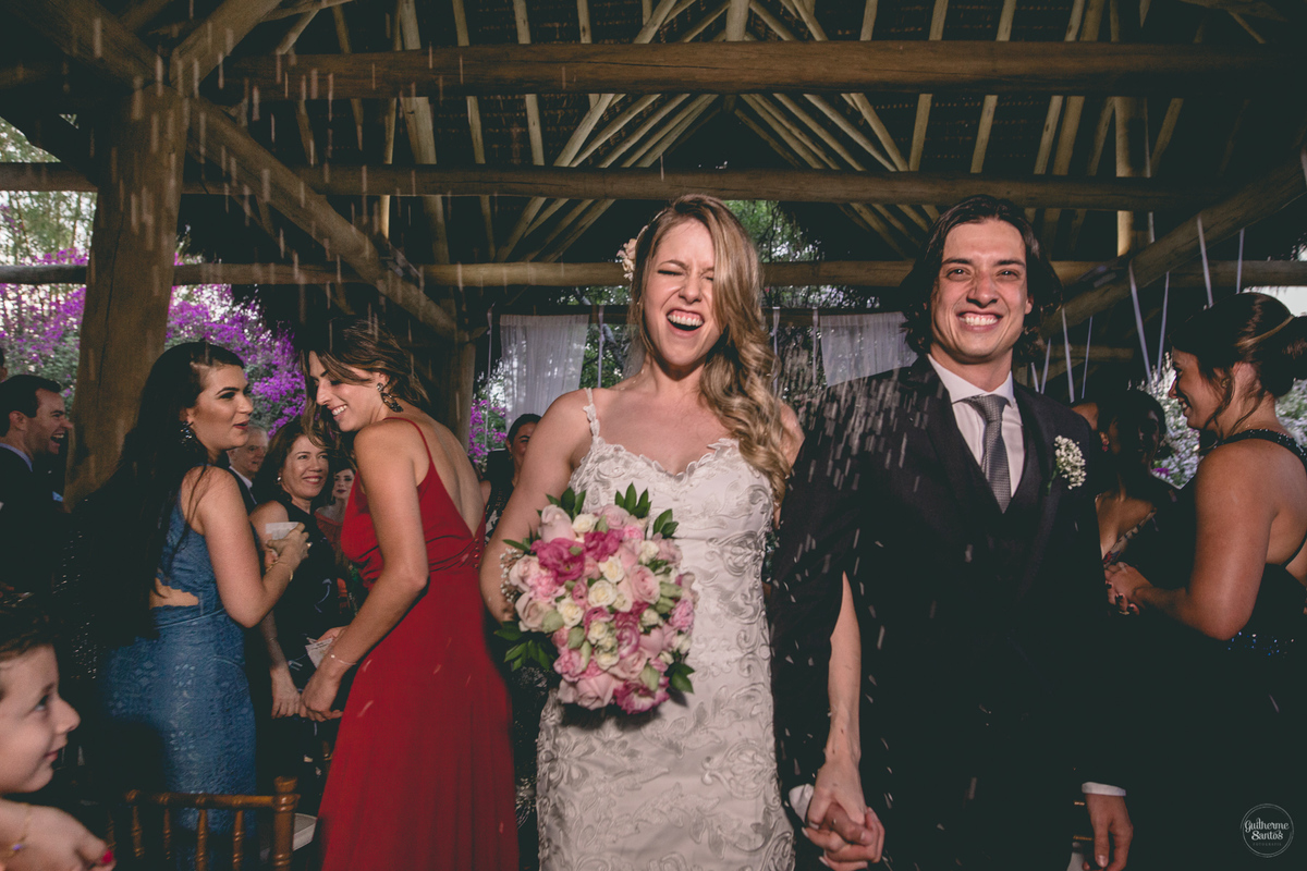 Fotografia de casamento feita no final de tarde pelo fotógrafo Guilherme Santos, noivos felizes recebendo chuva de arroz na saída do casamento ao ar livre em Botucatu.