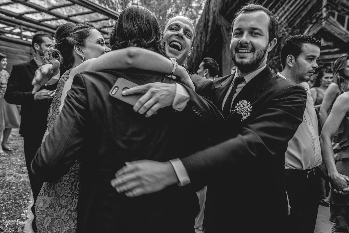 Fotografia de casamento feita no final de tarde pelo fotógrafo Guilherme Santos, padrinhos abraçando o noivo no casamento ao ar livre em Botucatu.