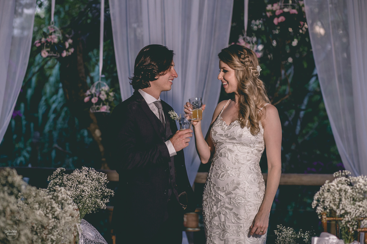 Fotografia de casamento feita no final de tarde pelo fotógrafo Guilherme Santos, casal de noivos bebendo cerveja artesanal após a cerimônia do casamento ao ar livre em Botucatu.
