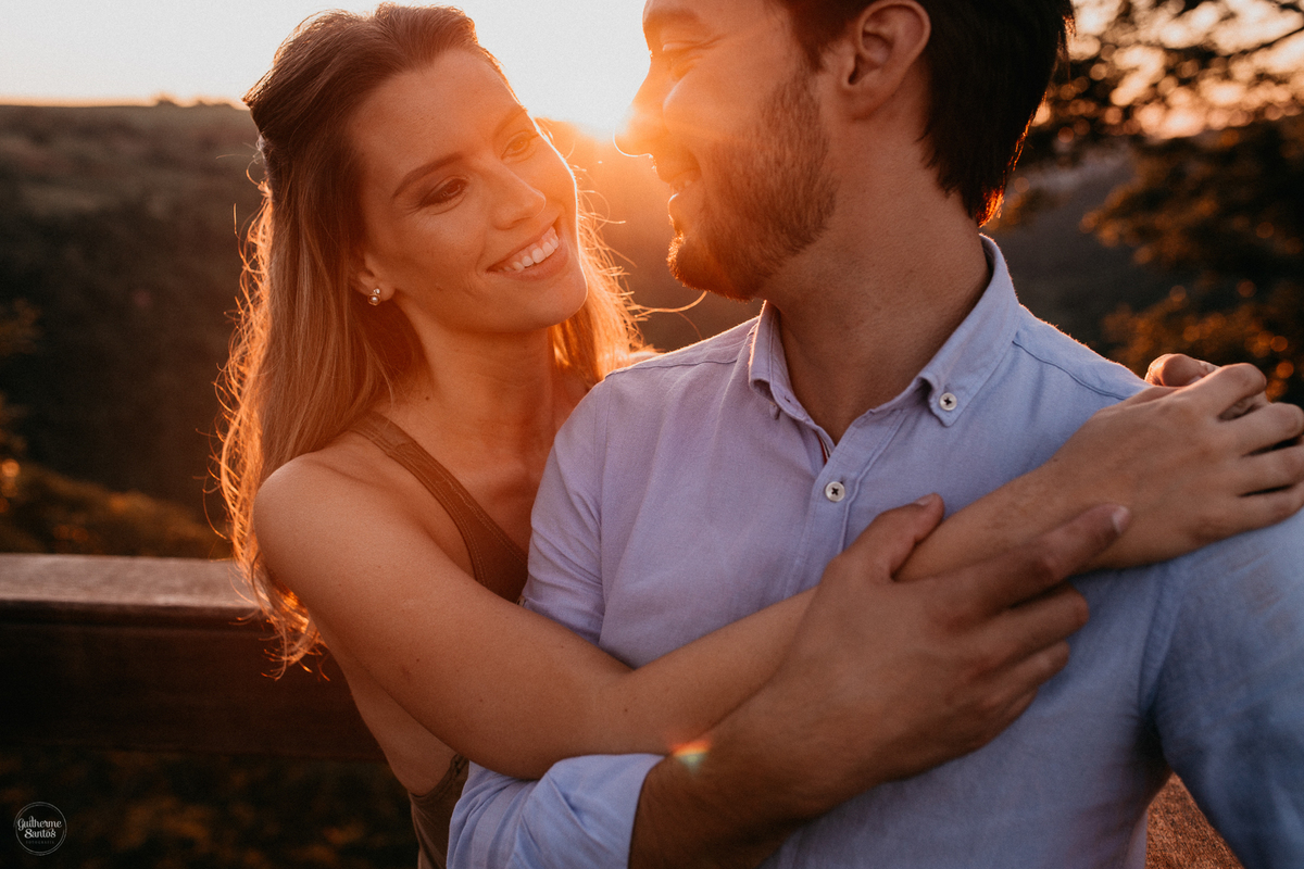 Fotografia de pré casamento feita no final de tarde pelo fotógrafo Guilherme Santos, casal de noivos felizes no pôr do sol na sessão pré casamento em Brotas. Os noivos estão se olhando, se abraçando e sorrindo,