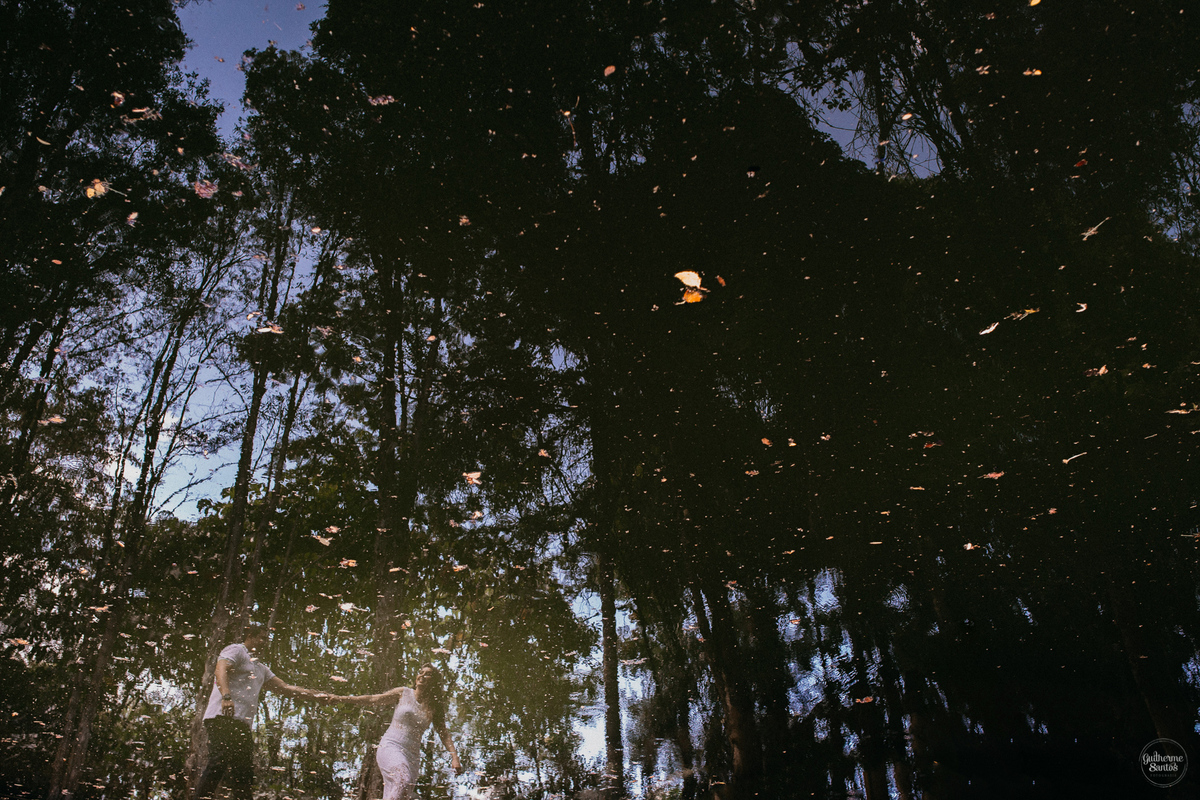 Fotografia de pré casamento feita no final de tarde pelo fotógrafo Guilherme Santos, casal de noivos caminhando durante a sessão de fotos de casamento, reflexo dos noivos na água.