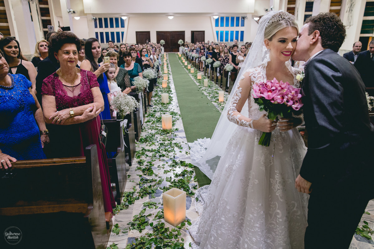 Fotografia de casamento pelo fotógrafo Guilherme Santos na região de Jaú Sp, Bauru Sp, Noivo beijando a noiva na cerimonia de casamento com os convidados olhando.