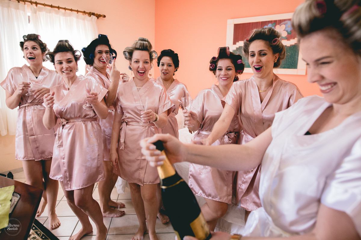 Fotografia de casamento pelo fotógrafo Guilherme Santos na região de Jaú Sp, Bauru Sp, Noiva com as madrinhas estourando uma champanhe em um quarto de hotel.