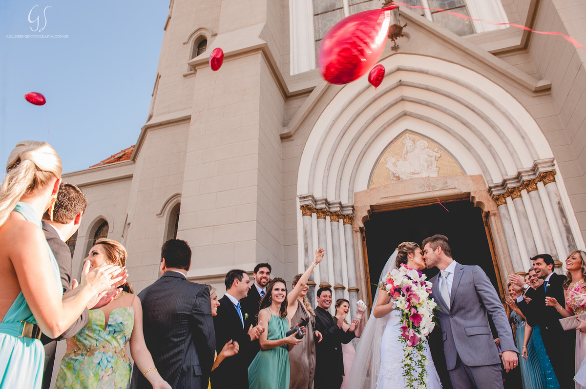 Fotografia de casamento pelo fotógrafo Guilherme Santos na região de Jaú Sp, Bauru Sp, final de cerimonia e os noivos se beijando e padrinhos sorrindo com balões de coração.
