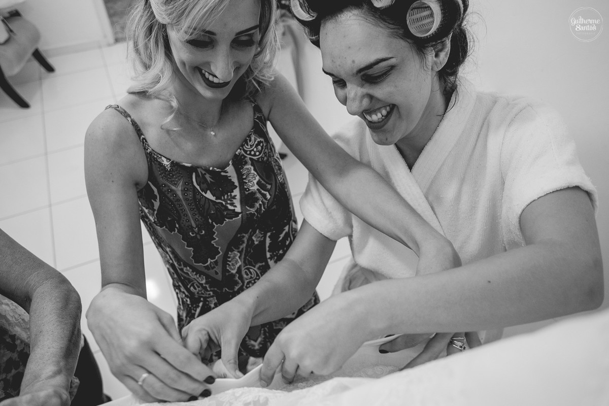 Fotografia de casamento pelo fotógrafo Guilherme Santos, noiva e sua irmão arrumando nome das madrinhas na barra do vestido
