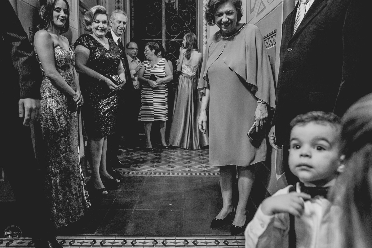 Fotografia de casamento pelo fotógrafo Guilherme Santos, convidados olhando e sorrindo para o pajem na porta da igreja