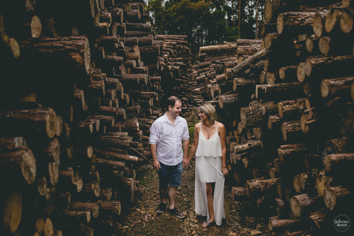 Ensaio pré casamento de Guilherme Santos Fotografia que rolou na Sengés-PR, sessão fotográfica no final de tarde. Noivos se olhando e sorrindo no meio de troncos de eucaliptos.