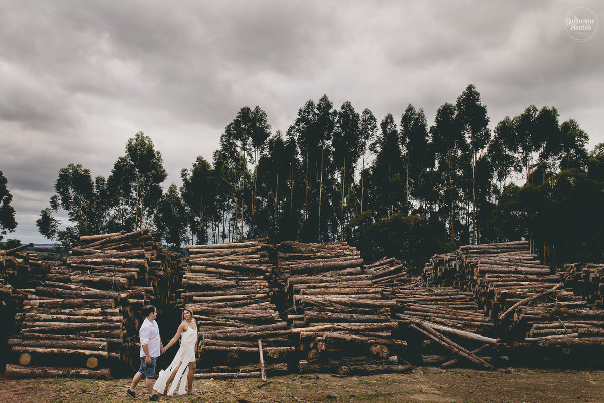 Ensaio pré casamento de Guilherme Santos Fotografia que rolou na Sengés-PR, sessão fotográfica no final de tarde. Noivos se olhando e sorrindo, correndo no meio de troncos de eucaliptos.