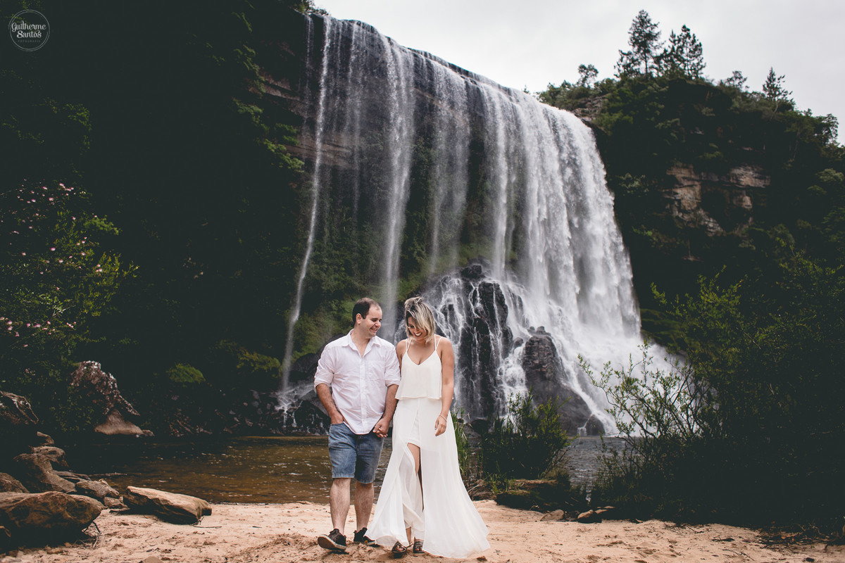 Ensaio pré casamento de Guilherme Santos Fotografia que rolou na Sengés-PR, sessão fotográfica no final de tarde. Noivos caminhando com a vista para uma cachoeira ao fundo.