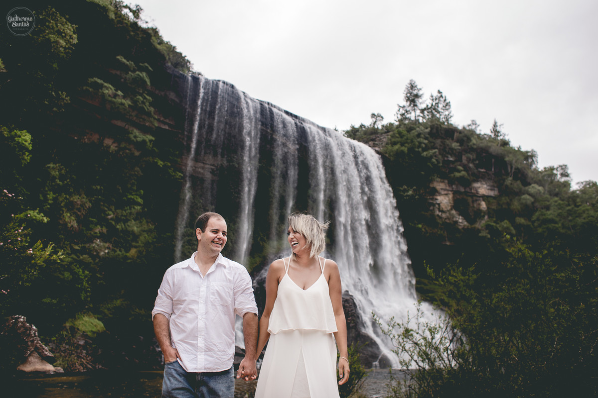 Ensaio pré casamento de Guilherme Santos Fotografia que rolou na Sengés-PR, sessão fotográfica no final de tarde. Noivos caminhando com a vista para uma cachoeira ao fundo.