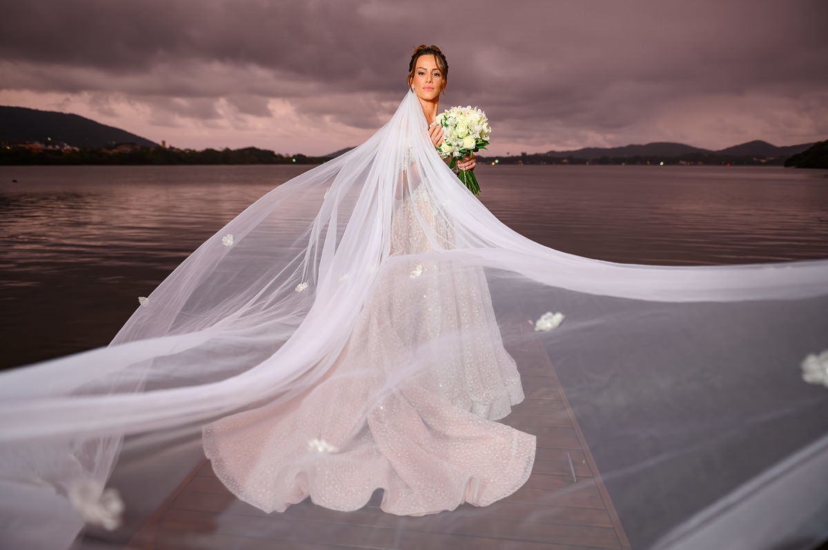 Retrato editorial da noiva Carolina com véu e céu dramático na Lagoa da Conceição