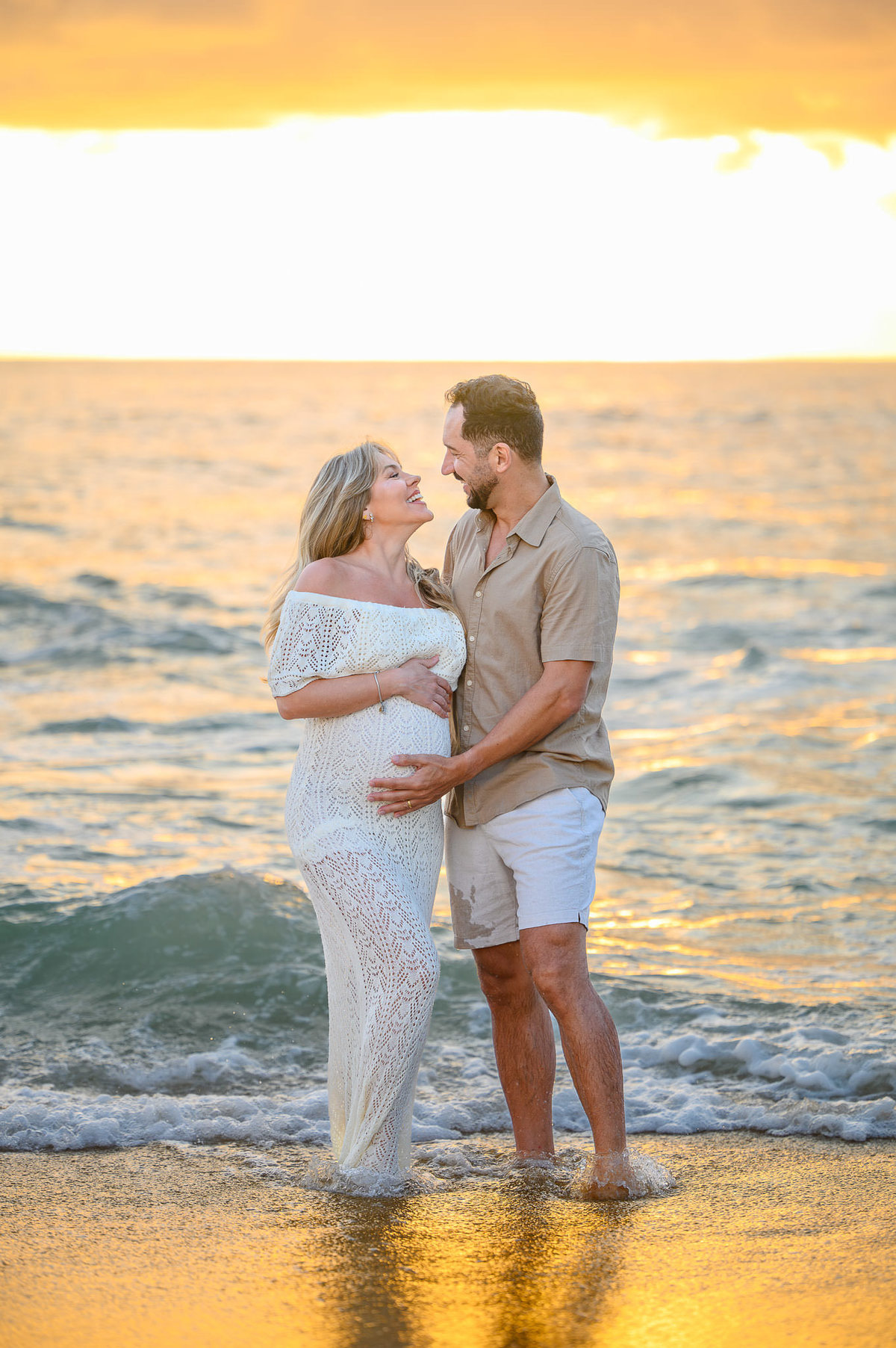 Casal em ensaio gestante ao amanhecer na Praia do Estaleirinho em Balneário Camboriú, com luz suave da manhã e mar ao fundo.