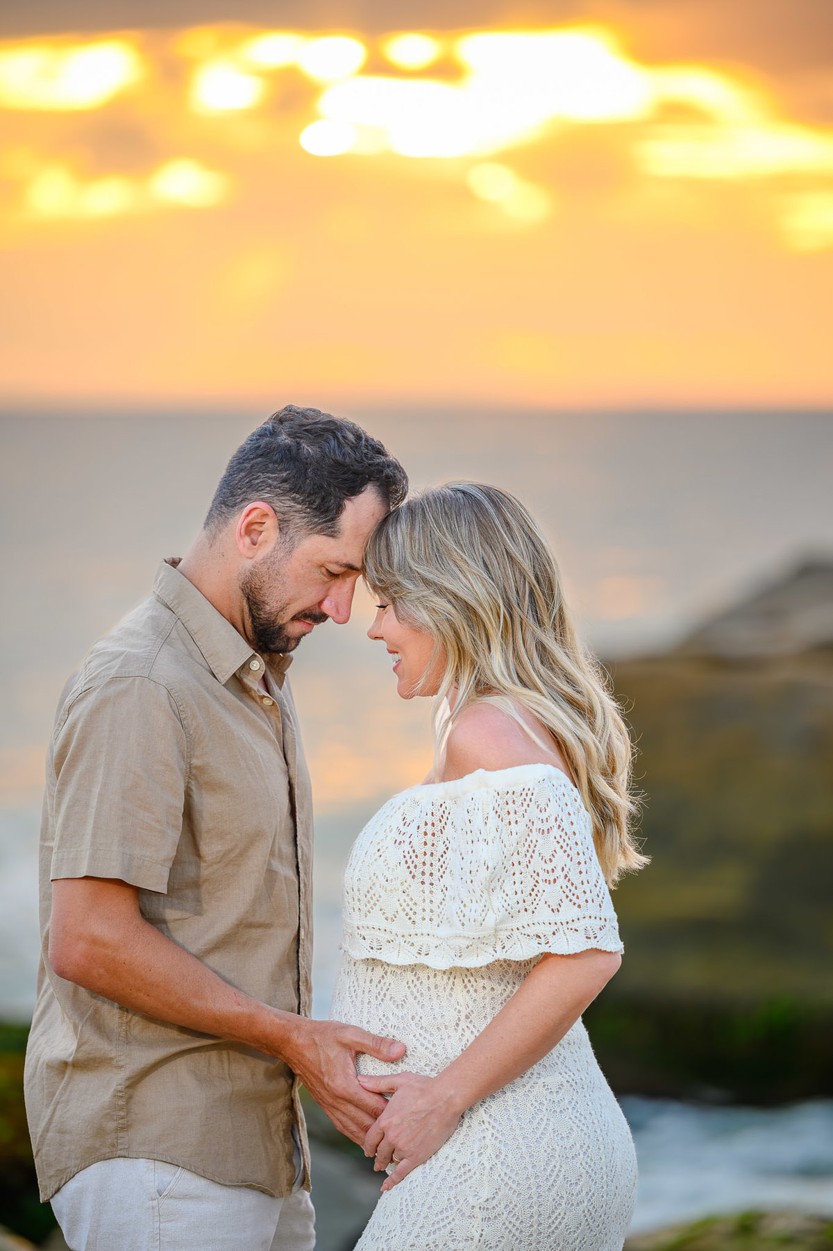 Gestante e parceiro em ensaio na Praia do Estaleirinho ao amanhecer, com mar calmo e luz natural da manhã.