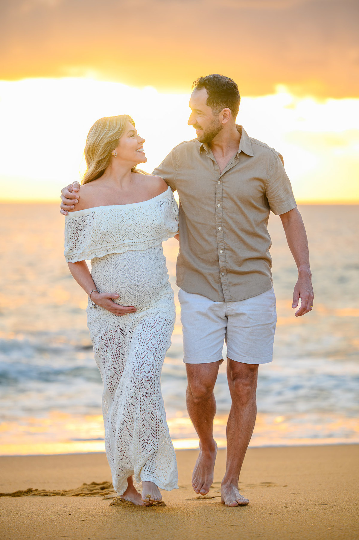 Ensaio fotográfico de gestante ao amanhecer em Balneário Camboriú com casal caminhando pela areia da praia.
