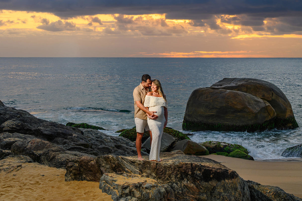 Casal em ensaio gestante ao amanhecer na Praia do Estaleirinho em Balneário Camboriú, com luz suave da manhã e mar ao fundo.