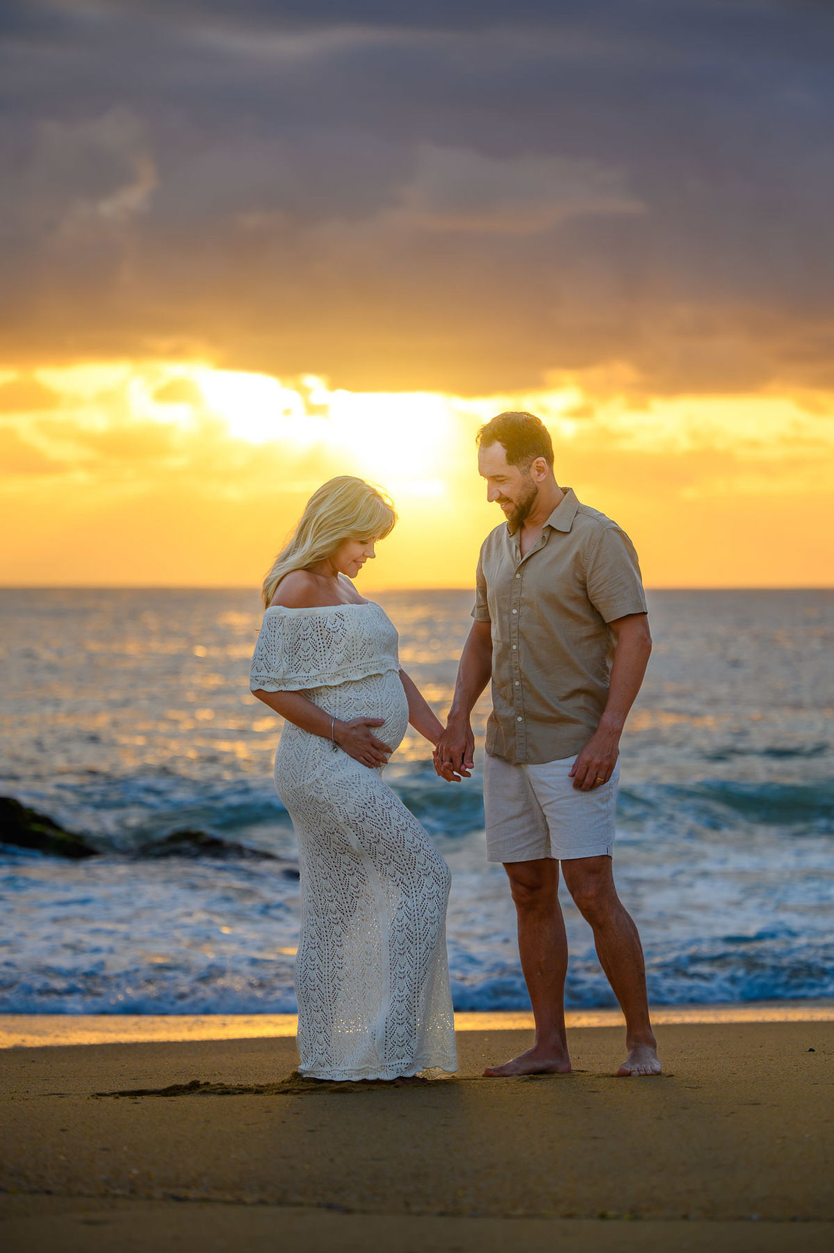 Gestante e parceiro em ensaio na Praia do Estaleirinho ao amanhecer, com mar calmo e luz natural da manhã.