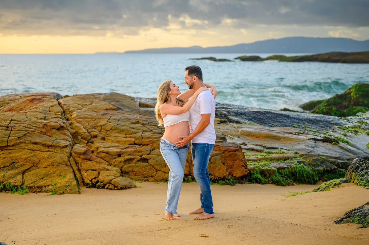 Fotografia de gestante em cenário de praia ao amanhecer em Balneário Camboriú, com casal em momento espontâneo.