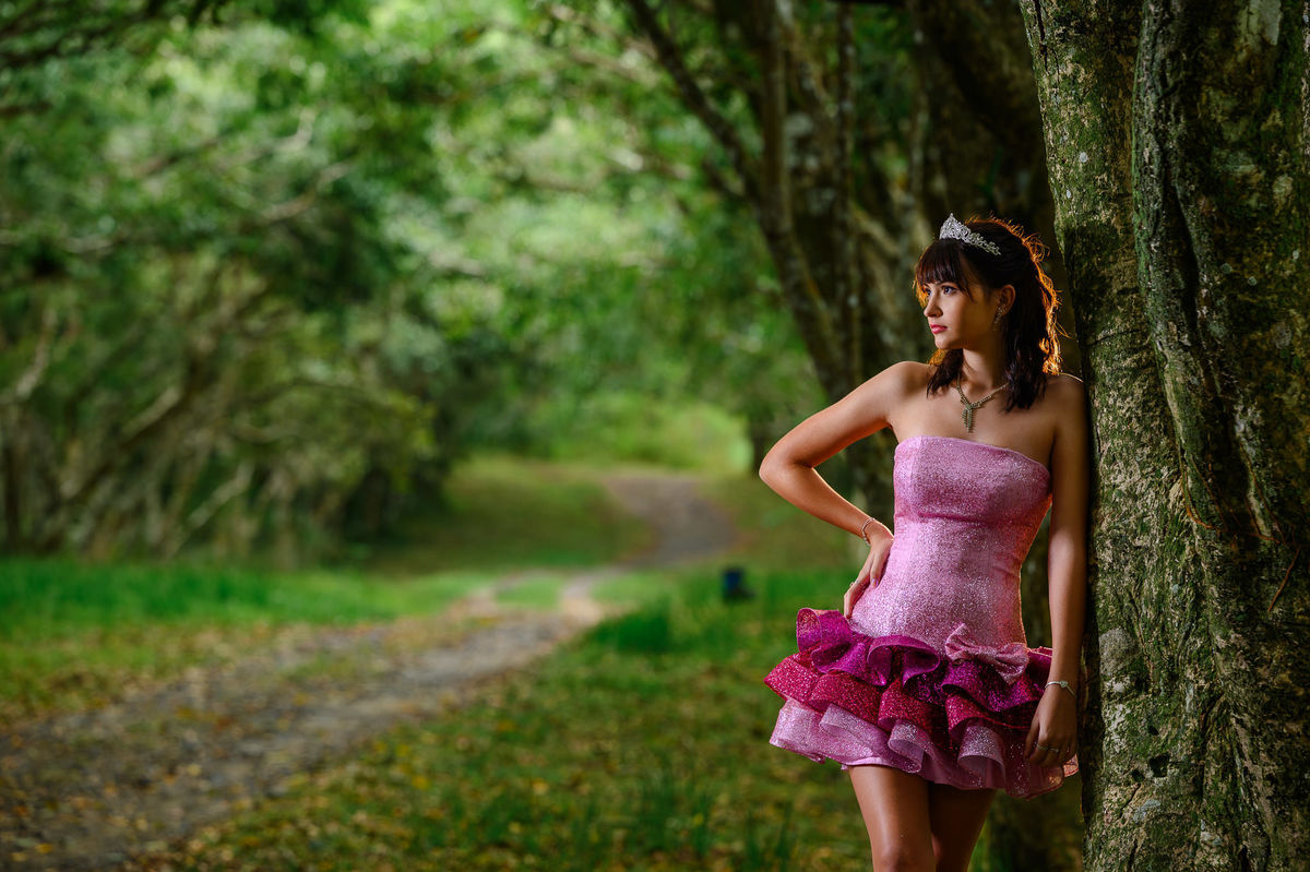 Ensaio de 15 anos em Balneário Camboriú com debutante em bosque, vestido rosa e coroa, em cenário natural