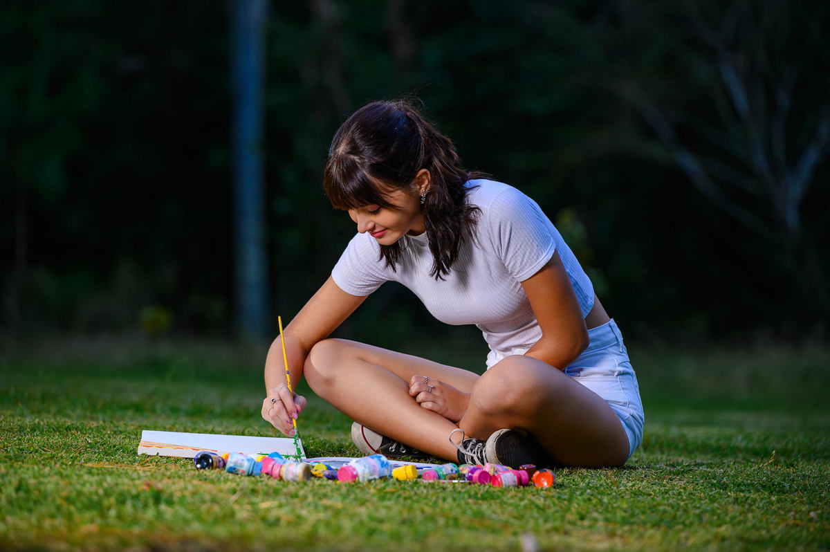 Debutante de 15 anos pintando tela no bosque em Balneário Camboriú SC durante ensaio fotográfico criativo ao ar livre