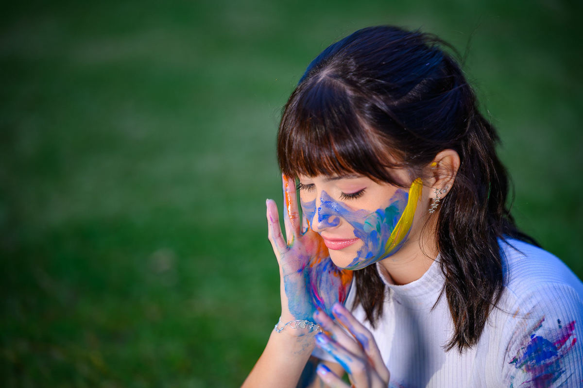 Retrato de debutante de 15 anos com tinta no rosto em ensaio fotográfico artístico em bosque de Balneário Camboriú SC
