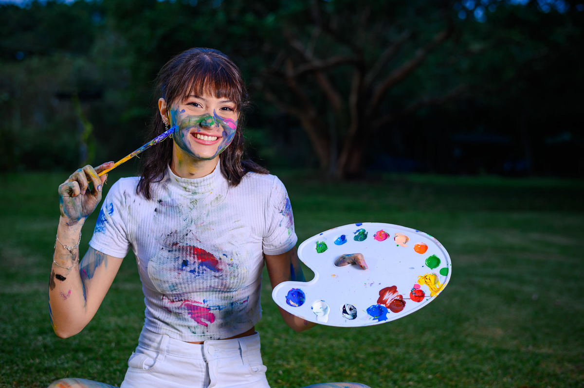 Ensaio de 15 anos em Balneário Camboriú SC com fotografia criativa de debutante segurando paleta de pintura ao ar livre