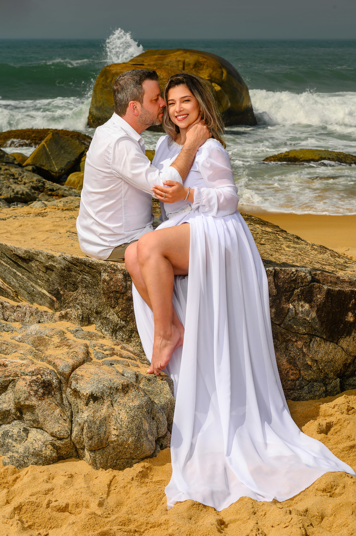 Fotografia de casal na Praia do Estaleirinho com mar agitado e rochas ao fundo