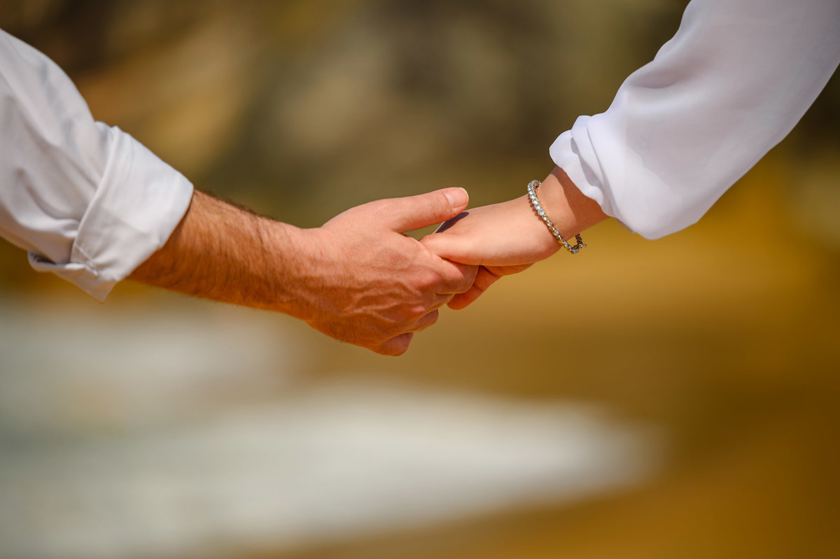 Detalhe das mãos do casal se tocando durante ensaio pré-wedding na praia