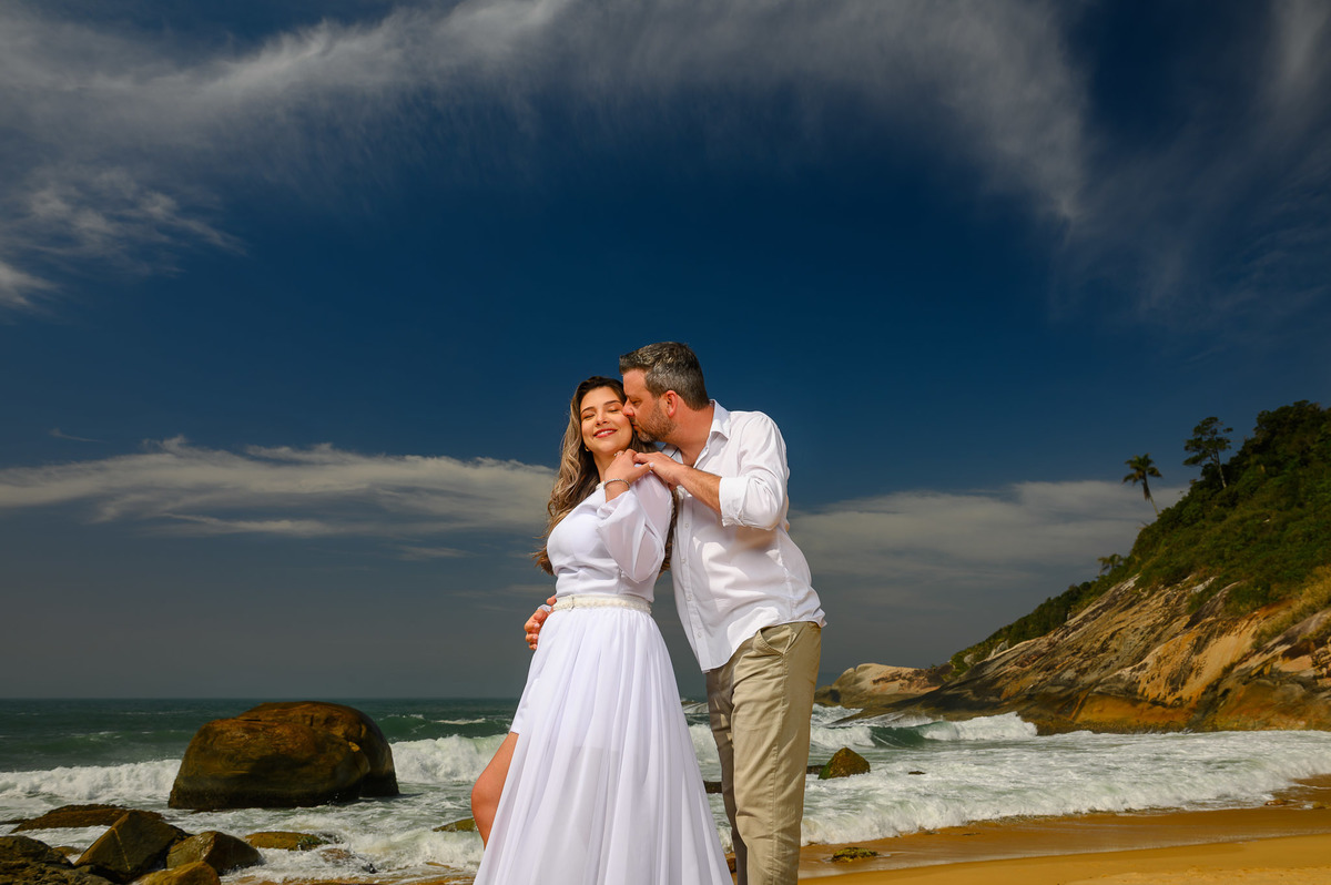 Ensaio de casal na praia em Balneário Camboriú, com céu dramático e ondas batendo nas pedras